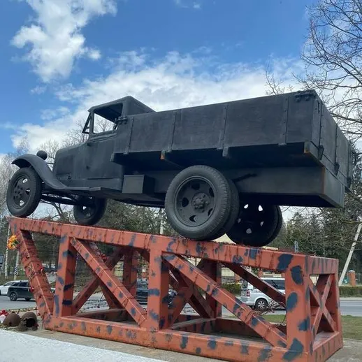 Памятник старому грузовику на постаменте в городском сквере под ясным небом