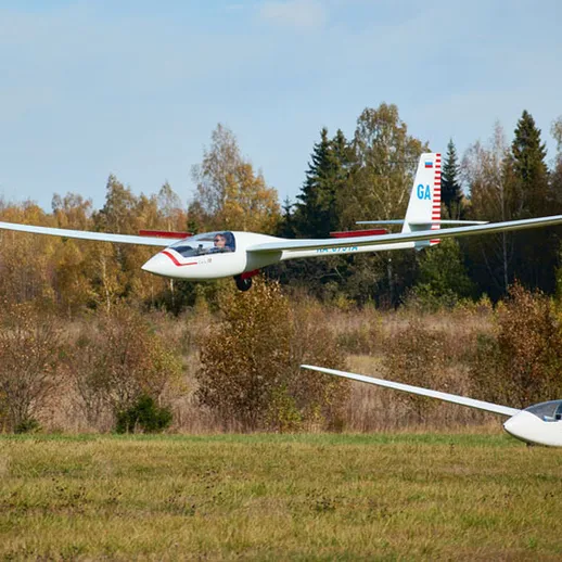 Летный день на аэродроме: две планера в небе и на земле среди осенних деревьев