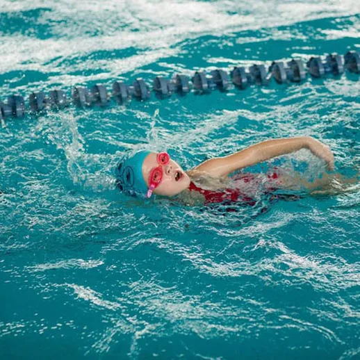 Девочка выполняет кроль на спине в бассейне во время тренировочного занятия