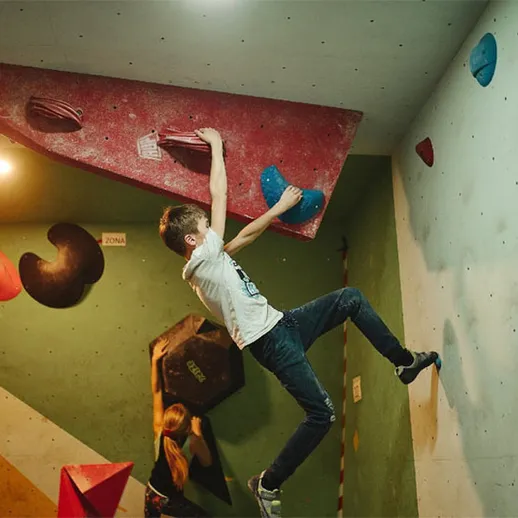 Подросток занимается скалолазанием в спортивном зале в вечернее время