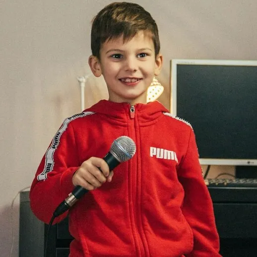 Мальчик поет с микрофоном в красной толстовке в домашней обстановке