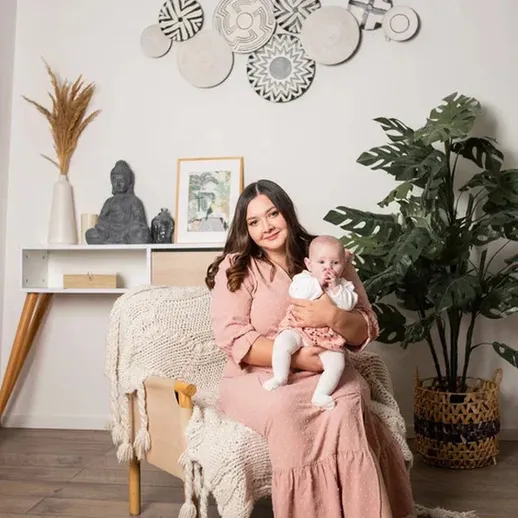 Мать держит малыша на руках в уютной комнате с растениями и декором