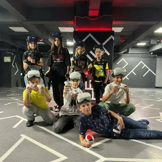 Дети играют в виртуальную реальность в игровом центре, восемь участников, помещение с современным дизайном, вечер