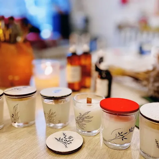 Ароматные свечи ручной работы на светлом деревянном столе в уютной комнате с теплыми оттенками и предметами шитья