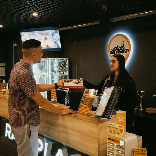 Молодой человек общается с сотрудником на стойке регистрации в развлекательном центре, вечером в городе