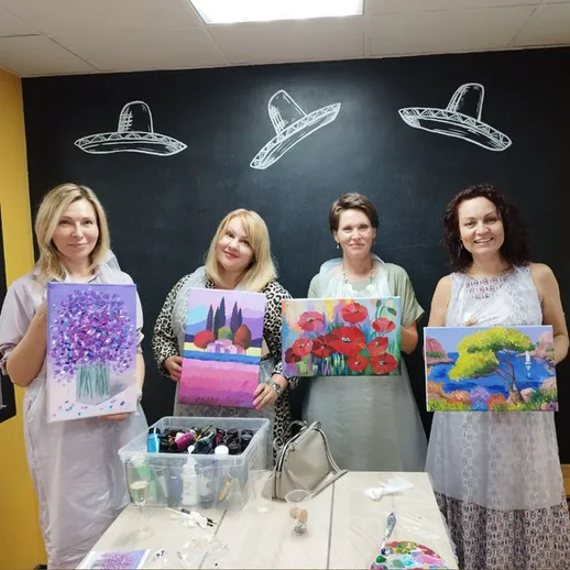 Четыре женщины показывают свои картины на мастер-классе по живописи в творческом пространстве