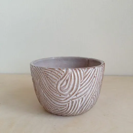 Керамическая чаша с извивающимся узором на ней, стоящая на столе в светлом помещении