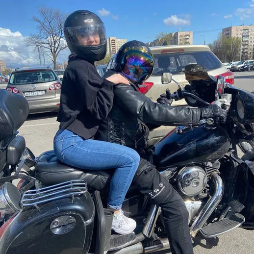 Молодая пара в защитных шлемах катается на мотоцикле в городском районе под солнечным небом весной