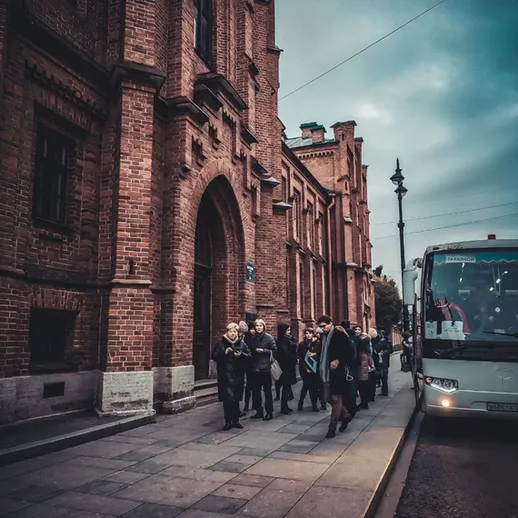 Группа людей выходит из автобуса в историческом здании в городе на закате