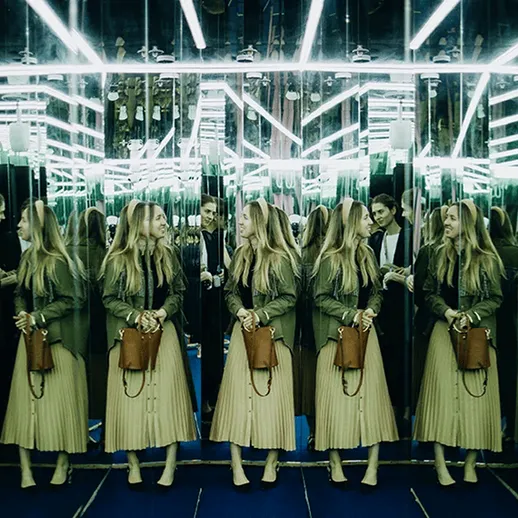 Группа людей обсуждают в зеркальном коридоре с ярким освещением, создающим эффект многократного отражения