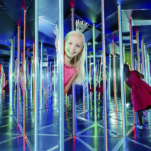 Девочка в зеркальном лабиринте с яркими огнями, играющая с отражениями в Москве