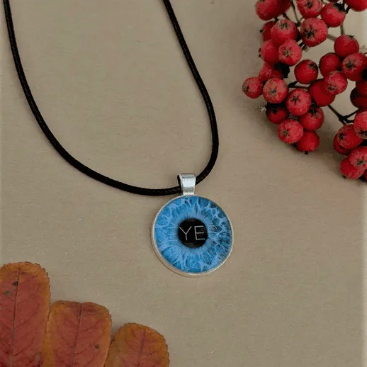 Подвеска с глазом и надписью на черном шнурке среди осенних листьев и рябины