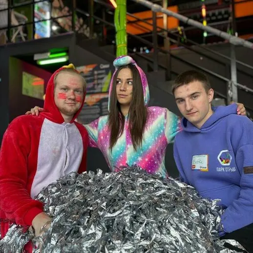 Группа друзей в необычных костюмах позирует у спортивной площадки с серебристым пушистым облаком