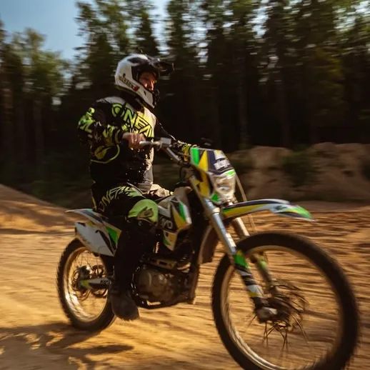 Мотоциклист в защитной экипировке на мотокроссе на песчаных трассах в лесу в солнечный день