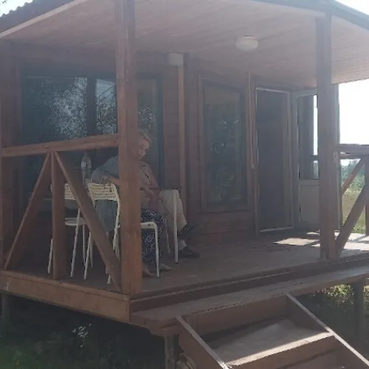 Домик на берегу реки с террасой и отдыхающим на стуле в солнечный день