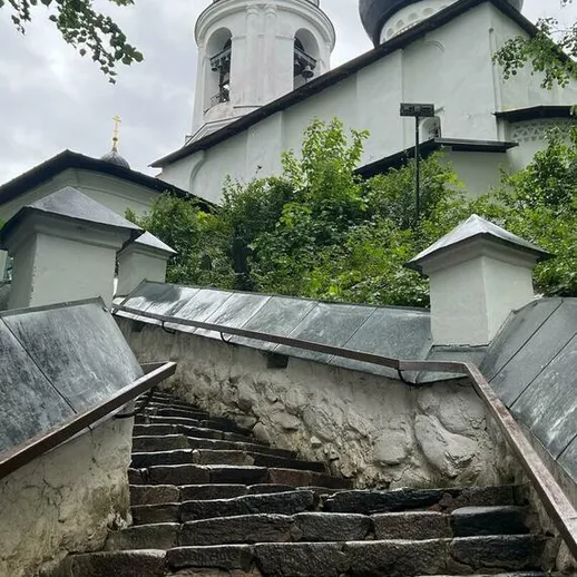 Подъем по каменистой лестнице к старинной церкви в зеленом окружении в ясный день