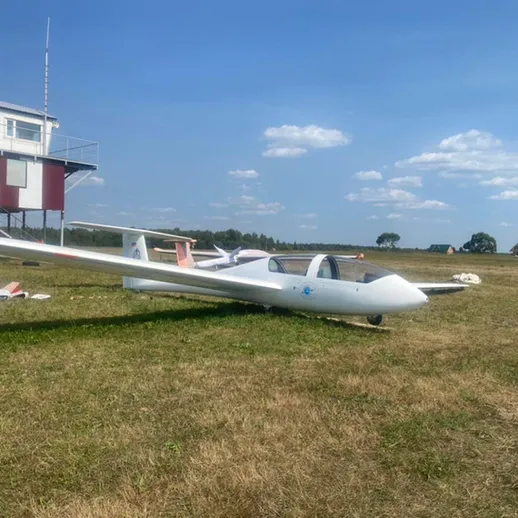 Белый планер стоит на траве рядом с аэропортом в солнечный день, готовый к полету для учебной тренировки