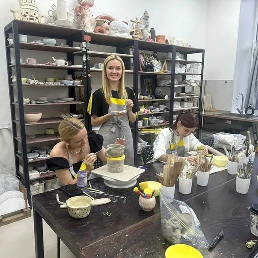 Занятие по гончарному делу в творческой мастерской, женщины создают керамические изделия с улыбками на лицах, уютная атмосфера