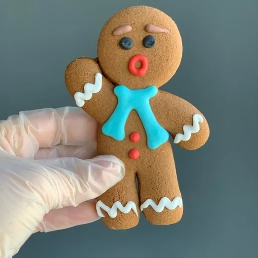 Имбирный пряник в форме человека с голубым шарфом и красными кнопками на фоне серого цвета