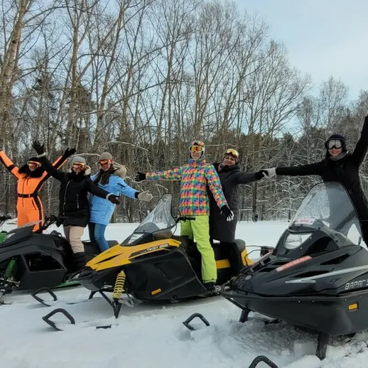 Группа людей на снегоходах в зимнем лесу, улыбаются и радуются активному отдыху