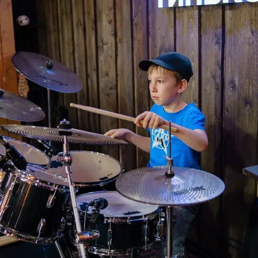 Мальчик играет на ударных в музыкальной студии во время репетиции
