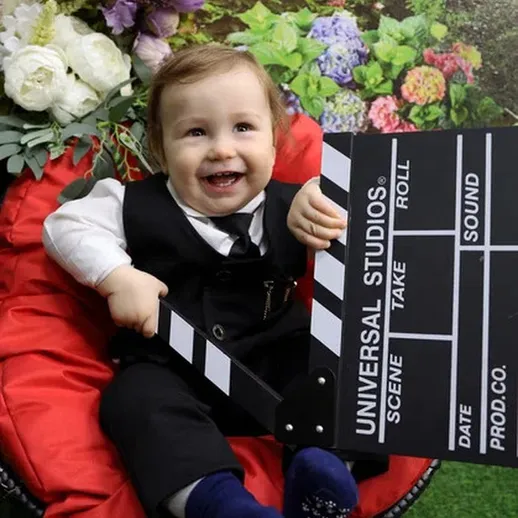 Маленький мальчик в черном костюме держит хлопушку на фоне цветов при праздновании дня рождения