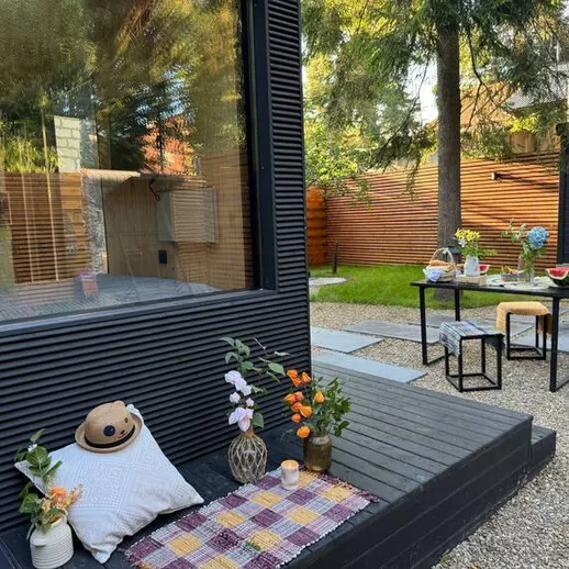 Уютная терраса в дачном доме с цветами и столом для ужина на фоне зелёного сада и зданий, утро в начале осени