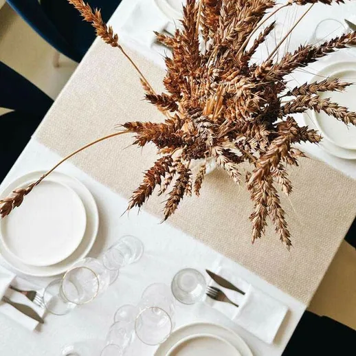 Уютный стол с белыми тарелками и сухими цветами в центре, готовый к обеденному времяпрепровождению в светлом помещении