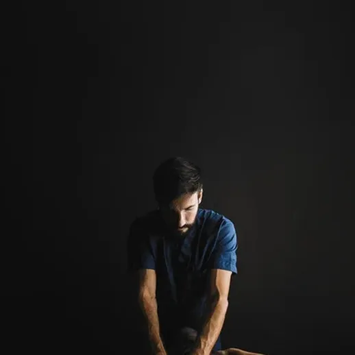 Массажист проводит расслабляющий массаж на фоне темной стены в спокойной обстановке