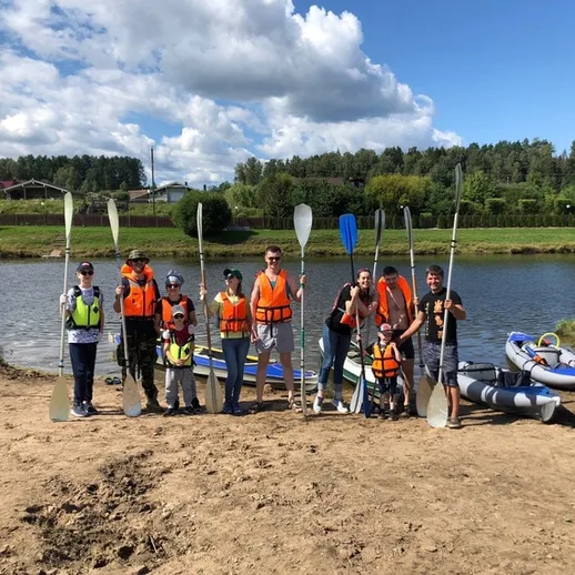Группа людей на водоёме с веслами, готовящаяся к сплаву по реке в солнечный день