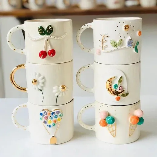 Красивая коллекция керамических кружек, украшенных ручной росписью, на белом столе