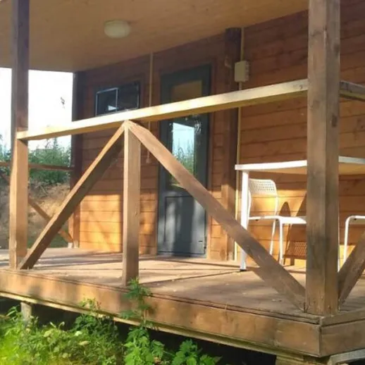 Деревянный домик с террасой в лесу на фоне зелени и солнечного дня