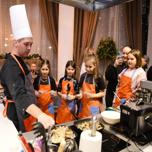 Шеф-повар обучает детей кулинарным навыкам на мастер-классе в уютном ресторане