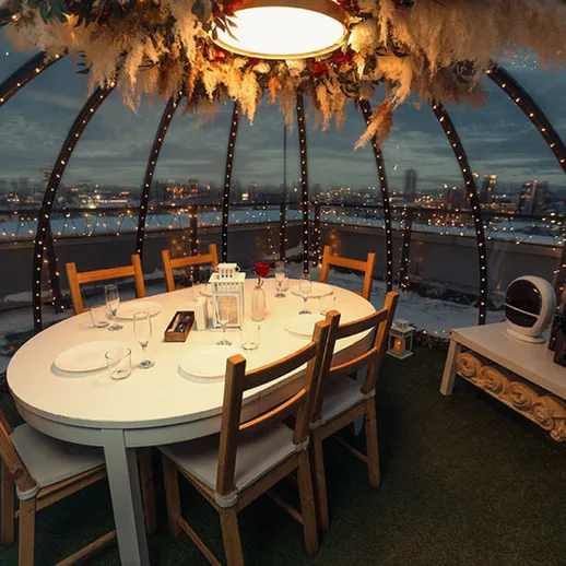 Зимний ужин в уютном стеклянном шатре с прекрасным видом на город в вечернее время