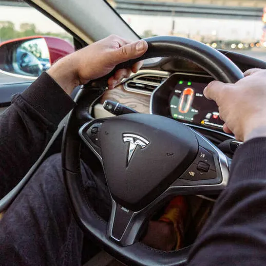 Водитель Tesla управляет автомобилем на улице города, солнечный день, вечернее время, комфортная атмосфера