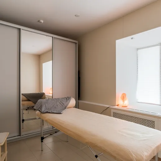 Уютный массажный кабинет с кроватью для процедур, большим окном и зеркальными шкафами