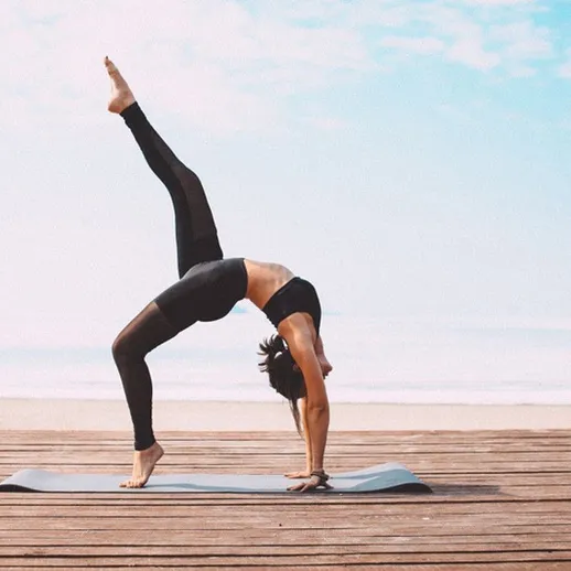 Занятие йогой на пляже в солнечный день, женщина выполняет асану с поддержкой одной ноги