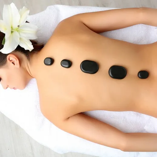 Женщина получает массаж с горячими камнями в спа-салоне среди белых полотенец и цветков