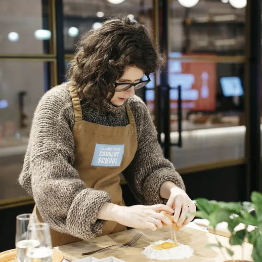 Женщина готовит на кухне, разбивая яйцо на тесто в учебном заведении по кулинарии