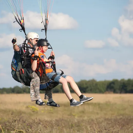 Парапланеристы приземляются на открытое поле в ясный день в летнее время