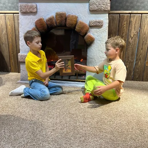 Дети играют у камина, передавая друг другу книгу в уютной комнате