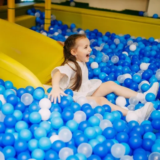 Девочка веселится на горке, играя в синем шаровом бассейне в игровом центре