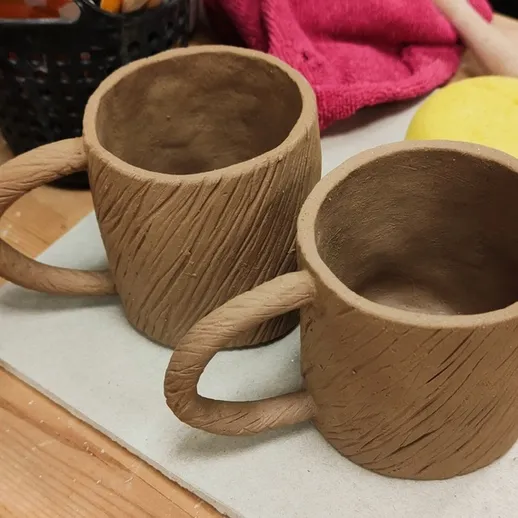 Глиняные кружки ручной работы на столе в мастерской во время урока творчества