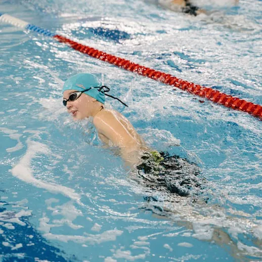 Пловец в шапочке и очках тренируется в бассейне с водой под ярким освещением