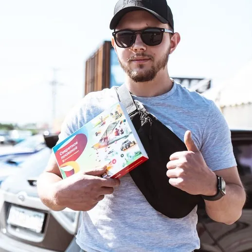 Мужчина с положительным жестом держит игру в упаковке на мероприятии на открытом воздухе в солнечный день