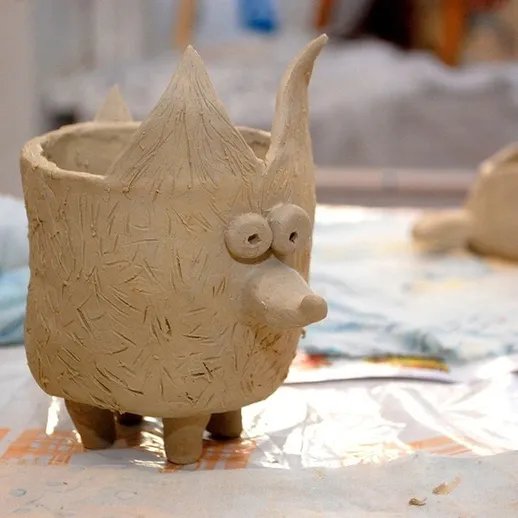 Глиняный горшок в виде животного с ушками и глазками на столе в мастерской ручной работы