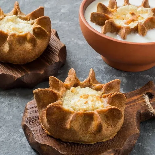 Вкусные вареники с начинкой на деревянной разделочной доске и тарелка сметаны на столе