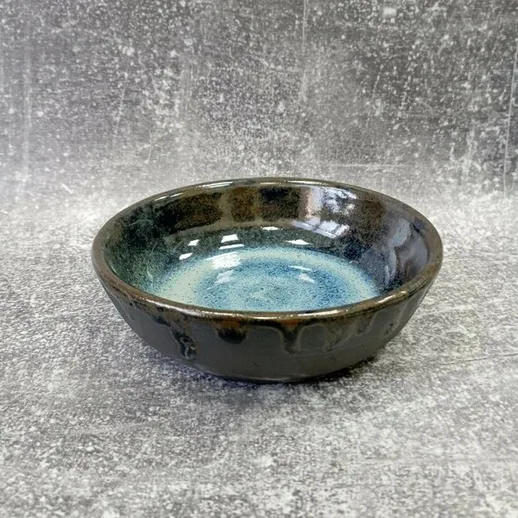 Керамическая чаша с голубой внутренней поверхностью на сером фоне, подходящая для сервировки или декора