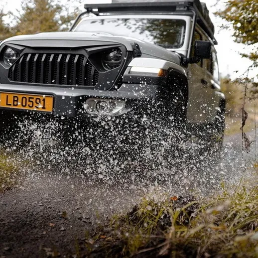 Внедорожник на грязной дороге в лесу, разбрызгивающий воду на скорости в солнечный день