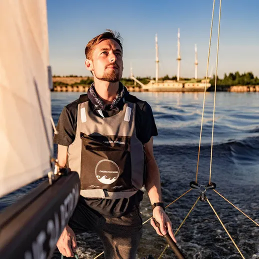 Молодой человек управляет парусной лодкой на спокойной воде в солнечный день